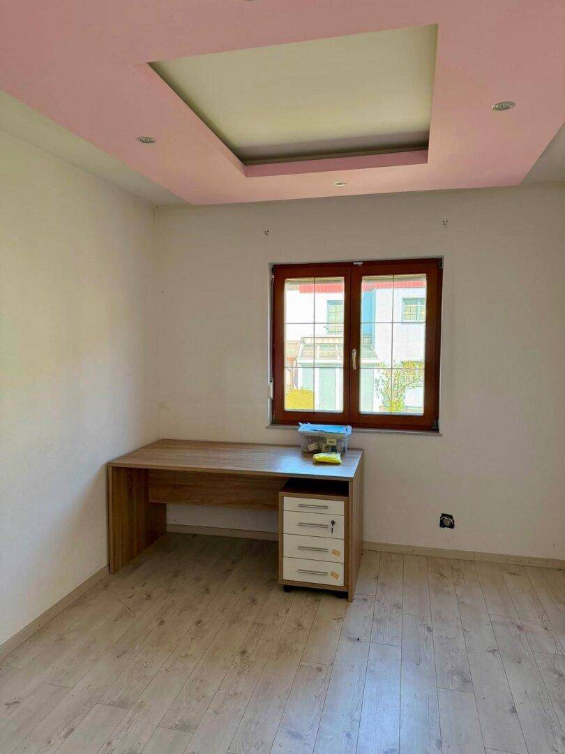 Helles Arbeitszimmer mit Schreibtisch, Laminatboden und modern gestalteter Decke.