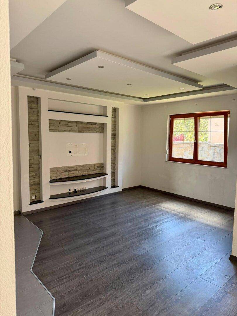 Geräumiges Wohnzimmer mit moderner Medienwand, Laminatboden und viel Tageslicht.