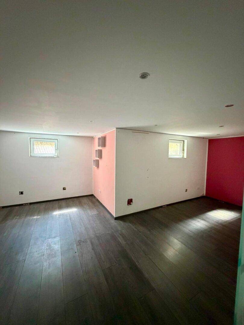 Vielseitig nutzbarer Raum im Untergeschoss mit Laminatboden und farbiger Akzentwand.
