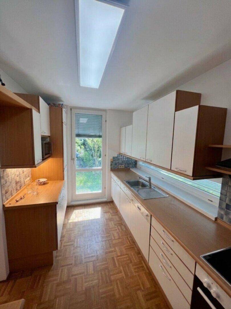 Helle, längliche Küche mit weißen Oberschränken, Holzarbeitsplatten und Fenster mit Gartenblick.