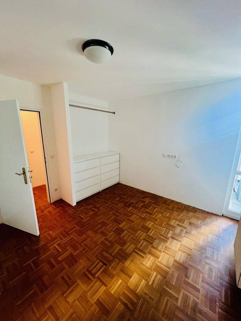 Schlafzimmer mit Parkettboden, weißem Wandschrank und Zugang zu einem kleinen Balkon oder französischen Fenster.