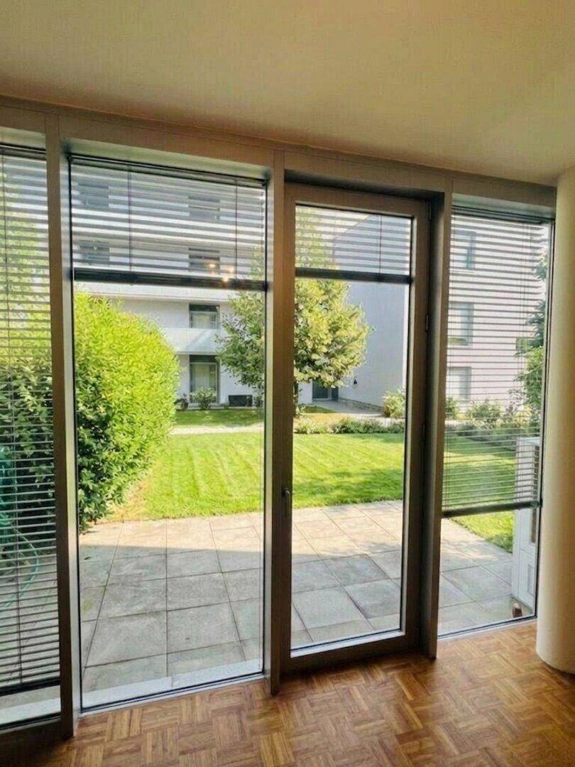 Heller Innenraum mit Parkettboden und großen Fenstern, die den Blick auf den grünen Garten freigeben.