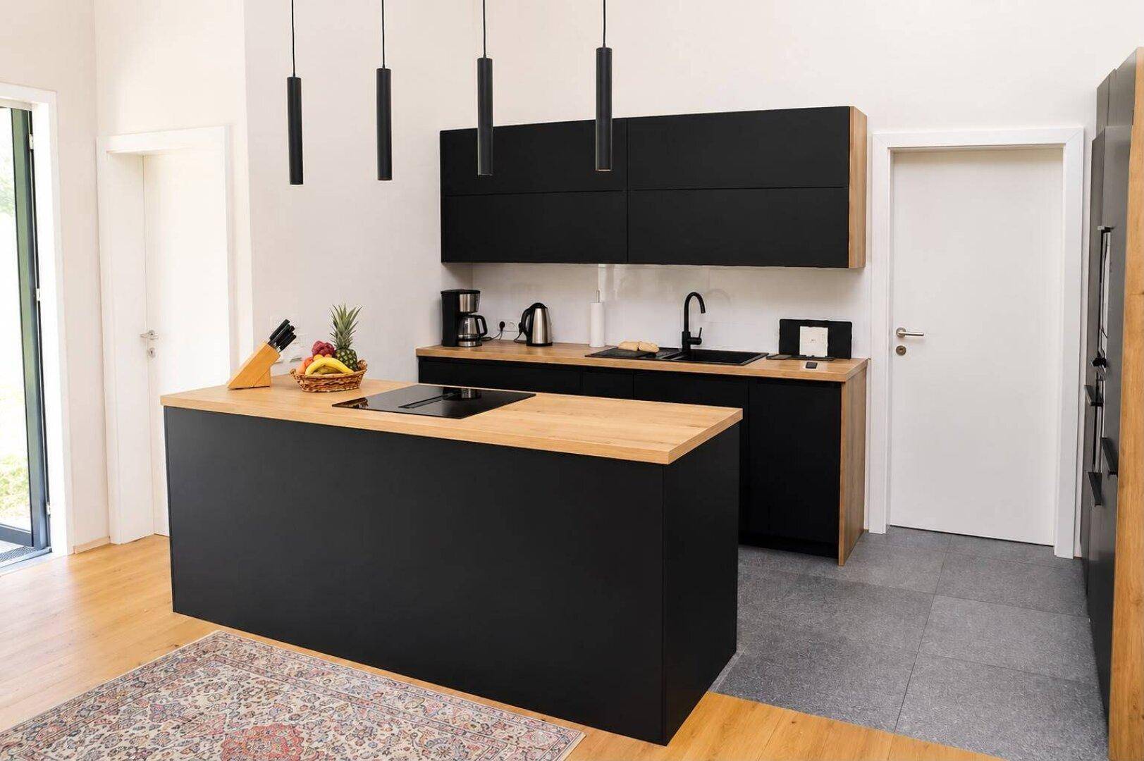 Moderne schwarze Küche mit Holz-Arbeitsplatten, Kücheninsel und Induktionskochfeld.