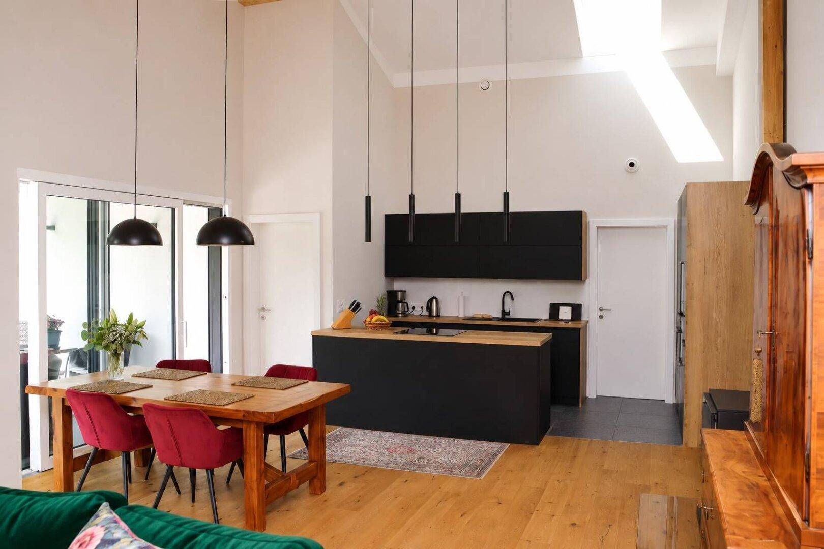 Offener Wohn- und Essbereich mit moderner Küche, hohen Decken und Zugang zur Terrasse.