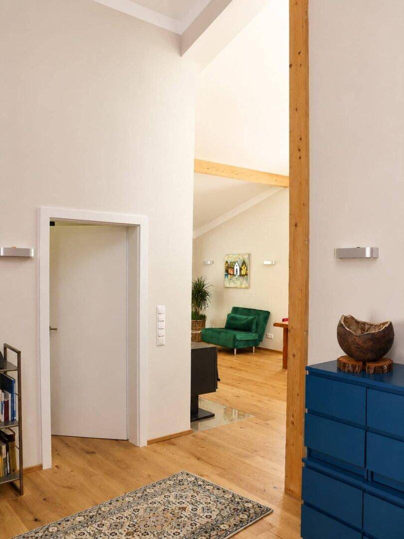 Heller Flur mit Holzbalken, Parkettboden und einem auffälligen blauen Sideboard.