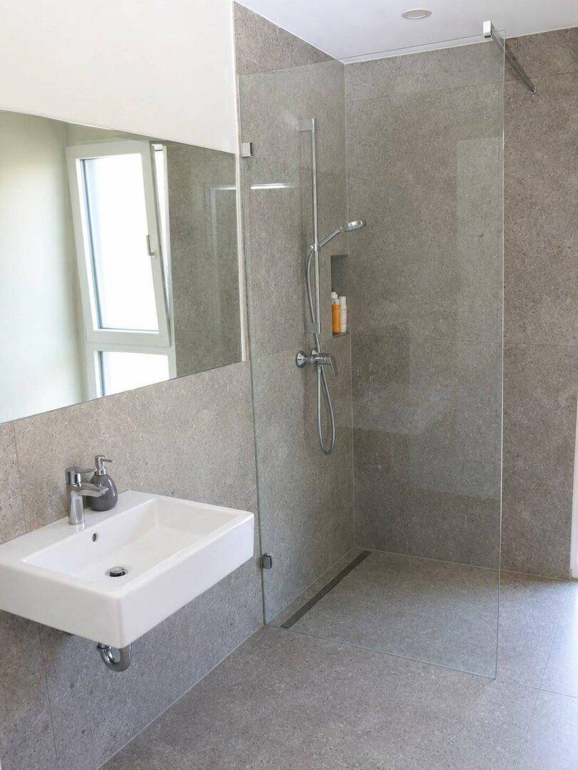 Modernes Badezimmer mit großer begehbarer Dusche, grauen Fliesen und Einzelwaschbecken.