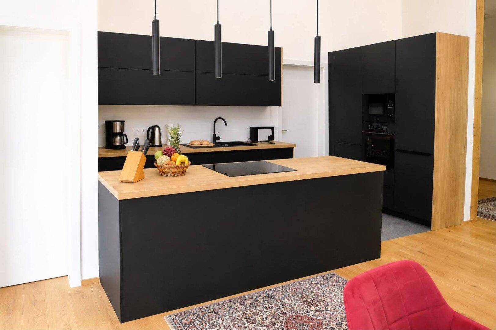 Stilvolle schwarze Küche mit Holz-Arbeitsplatten, Kücheninsel und integrierten Geräten.