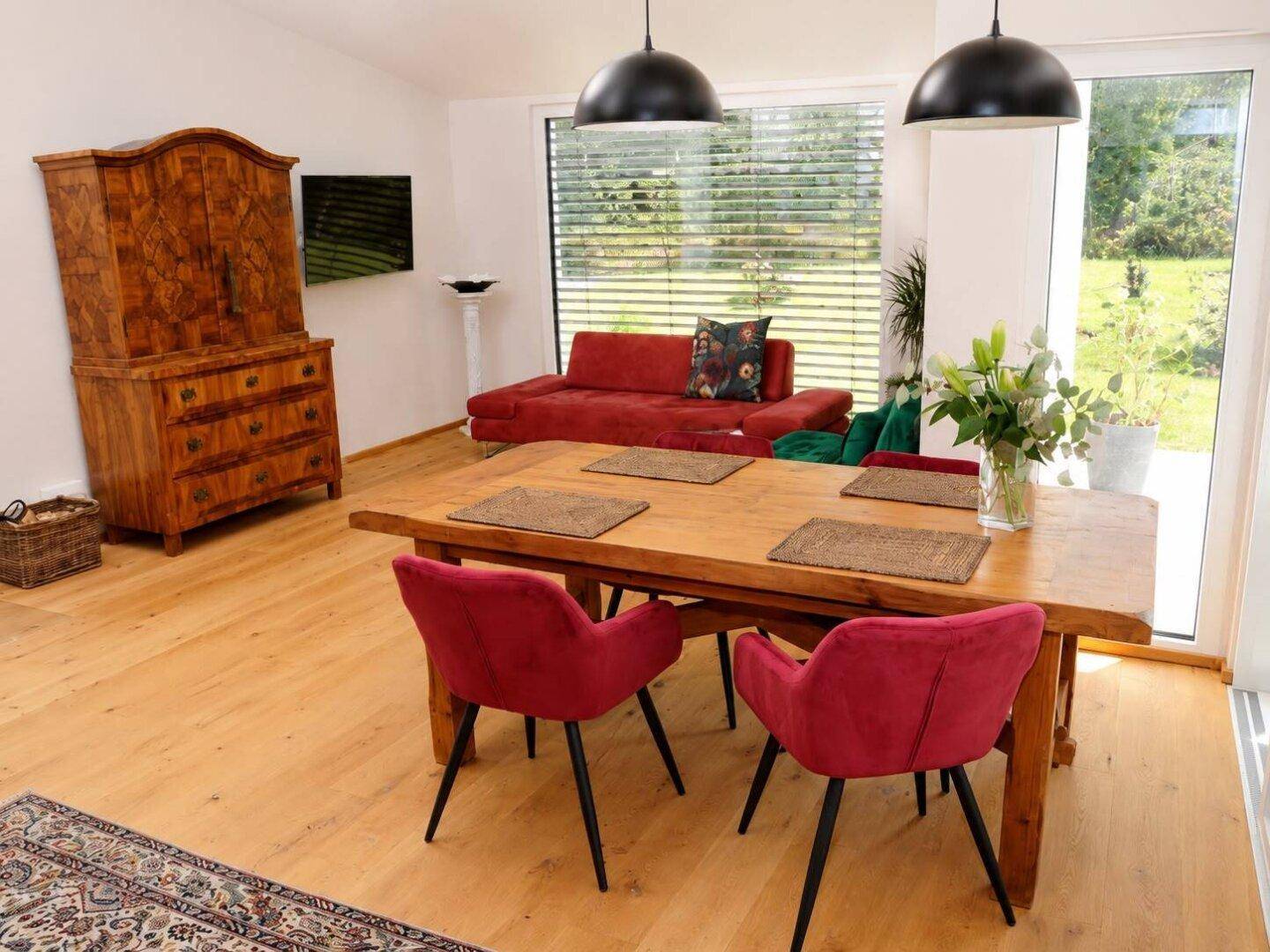 Gemütlicher Essbereich mit großem Holztisch, roten Stühlen und Blick ins Grüne.