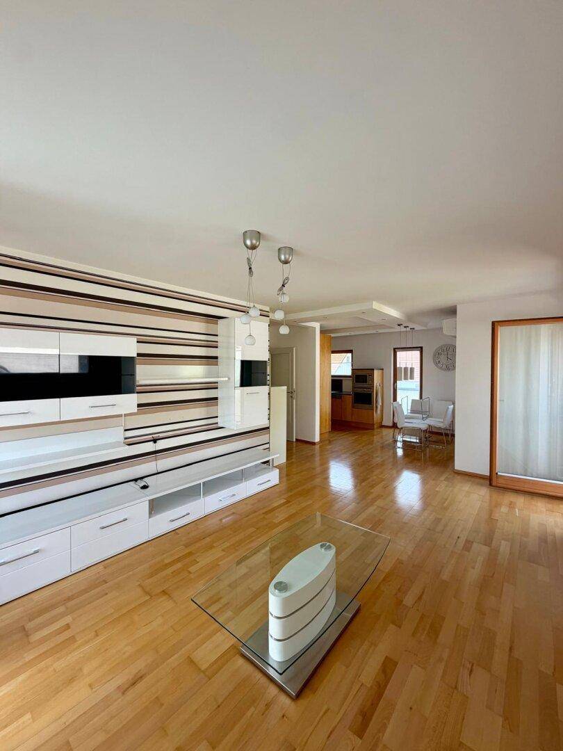 Geräumiges Wohnzimmer mit Parkettboden, moderner Wandgestaltung und Blick in den Essbereich.