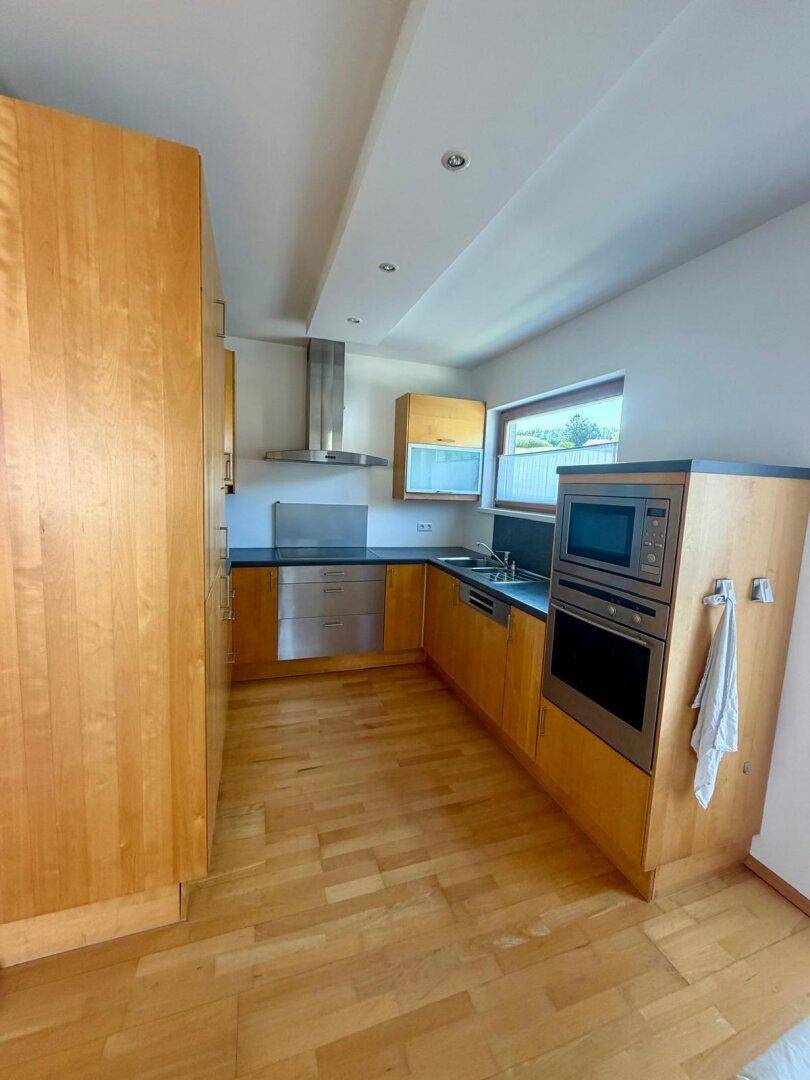 Funktionale Küche mit Holzschränken, Edelstahlgeräten und Parkettboden.
