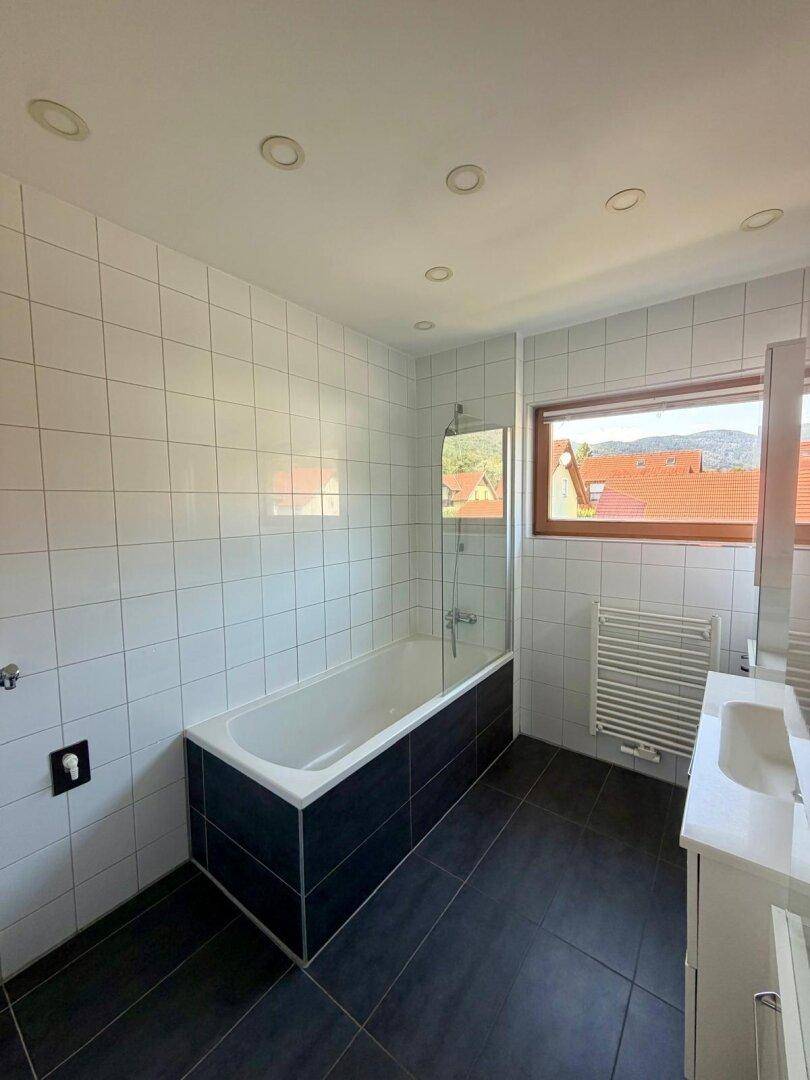 Modernes Badezimmer mit Badewanne, dunklen Bodenfliesen und Fenster.