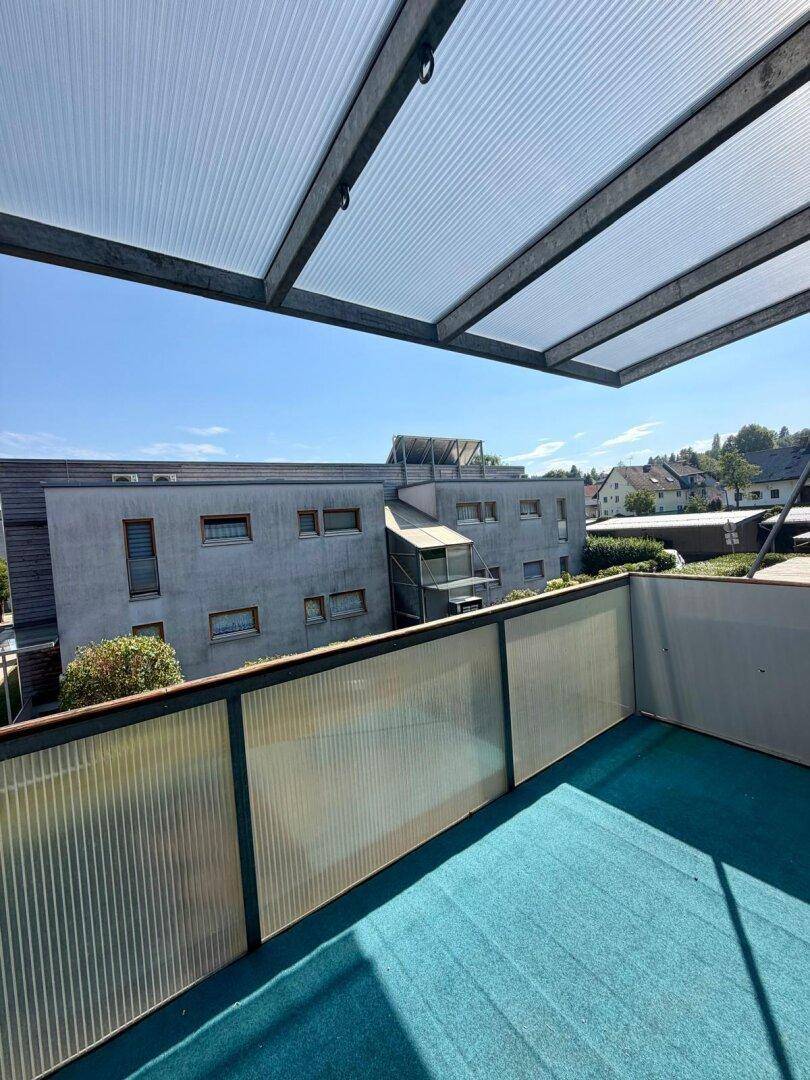 Überdachter Balkon mit Blick auf die umliegenden Gebäude und Grünflächen.