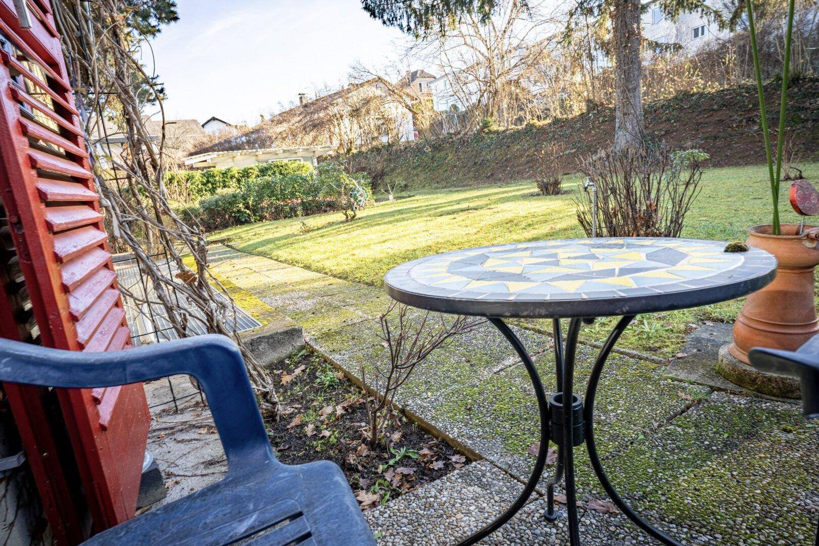 Gemütlicher Terrassenbereich mit Mosaiktisch und Sitzgelegenheiten, umgeben von Grün.