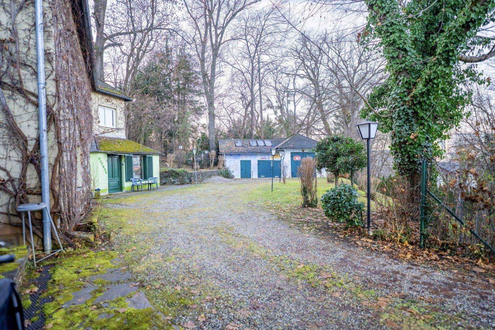 Zufahrt zum Haus mit Kiesweg und Blick auf Nebengebäude und den Gartenbereich.