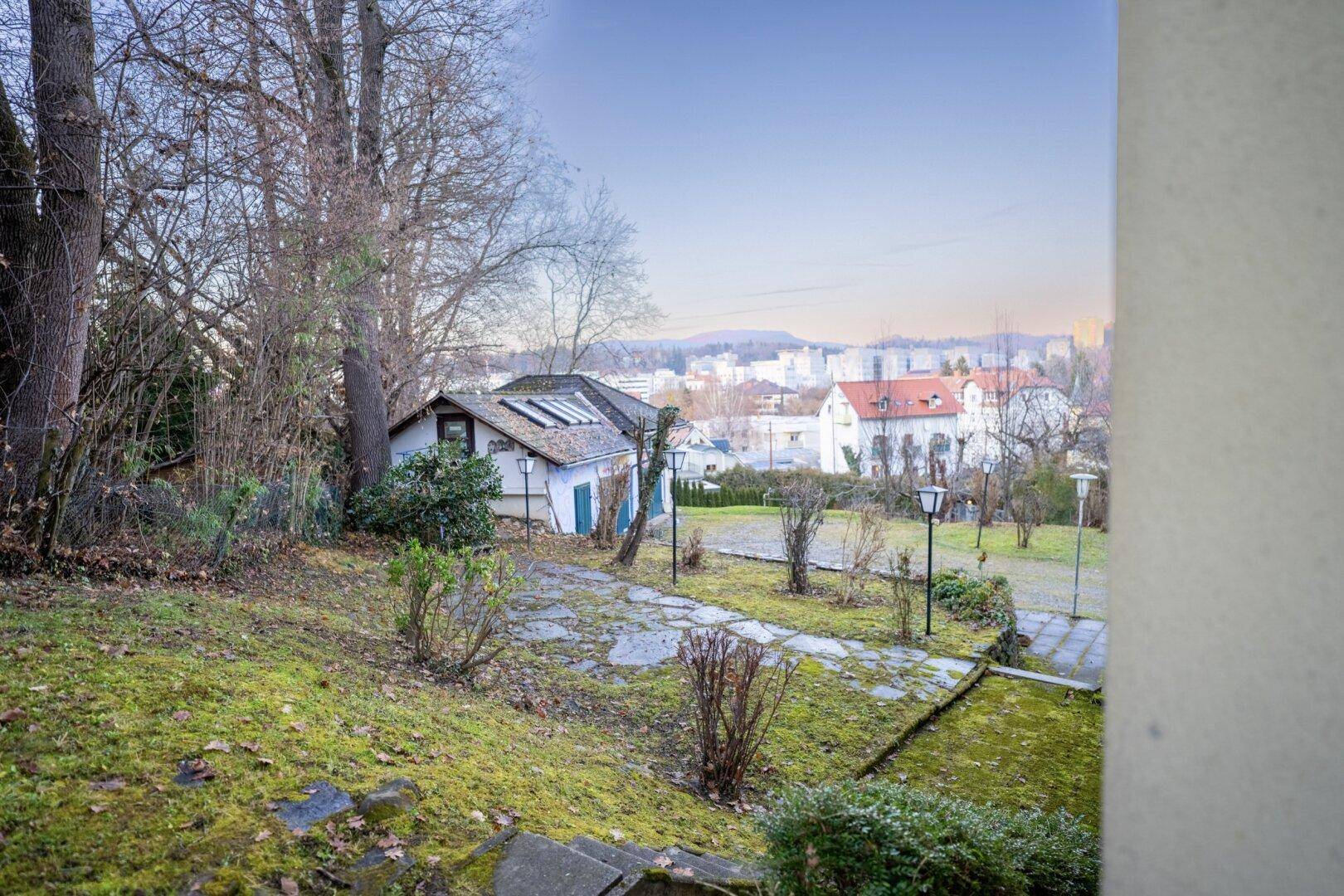 Erhöhter Blick über den Gartenbereich mit Nebengebäude und Panorama der Stadt.