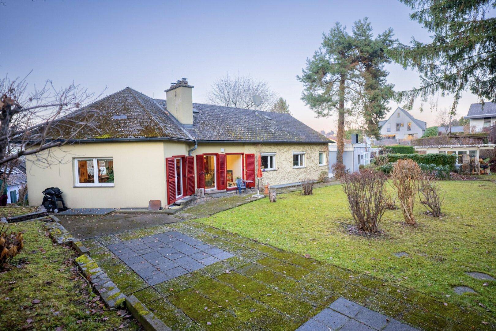 Rückseite des Hauses mit großer gepflasterter Terrasse und weitläufigem Rasenbereich.