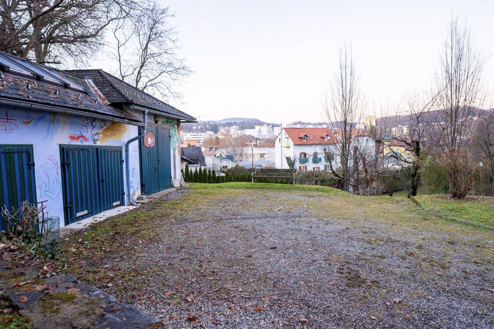 Nebengebäude mit farbenfroher Bemalung und Schotterfläche, mit Stadtblick im Hintergrund.