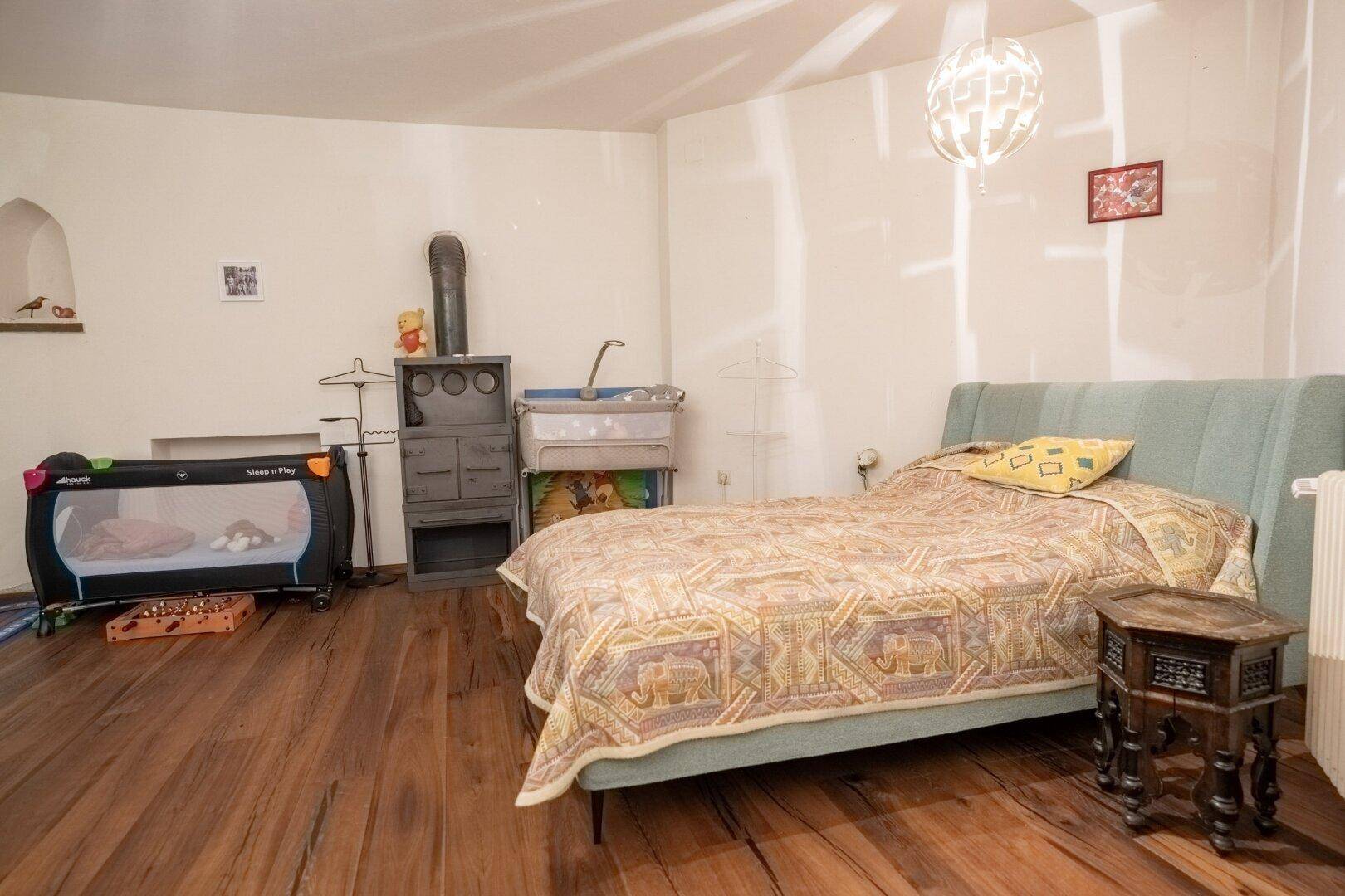 Gemütliches Schlafzimmer mit Holzboden, Doppelbett, Babybett und traditionellem Ofen.