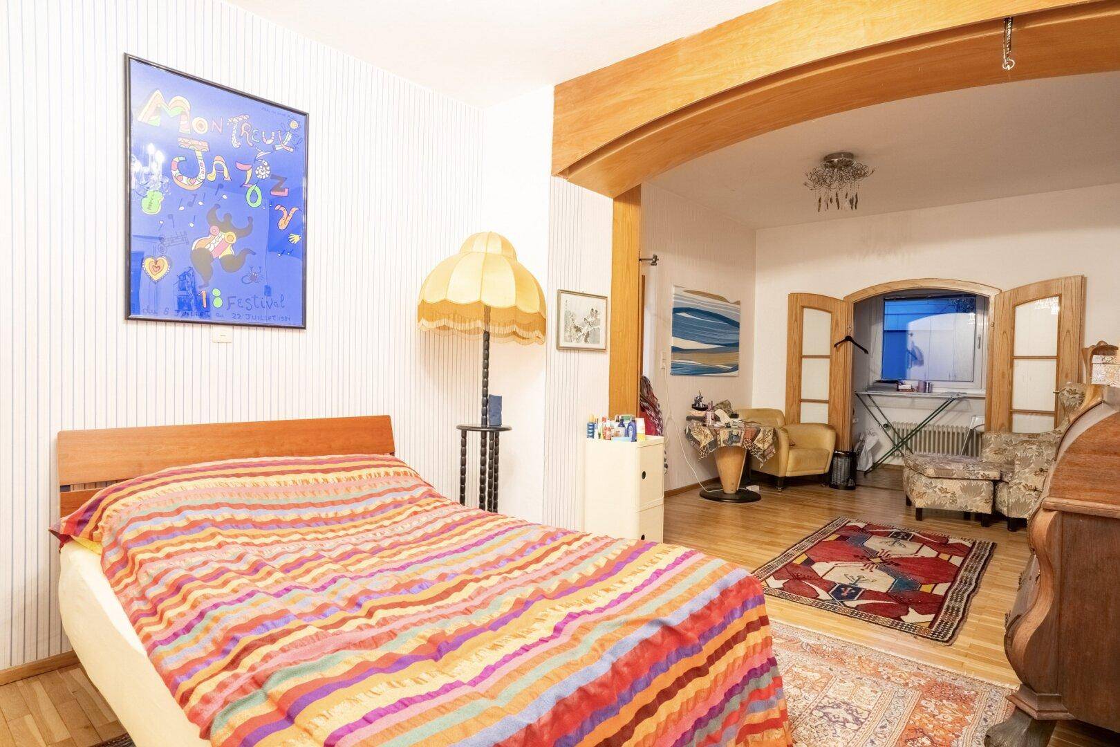 Schlafzimmer mit farbenfroher Bettwäsche und offenem Zugang zu einem angrenzenden Wohnbereich.