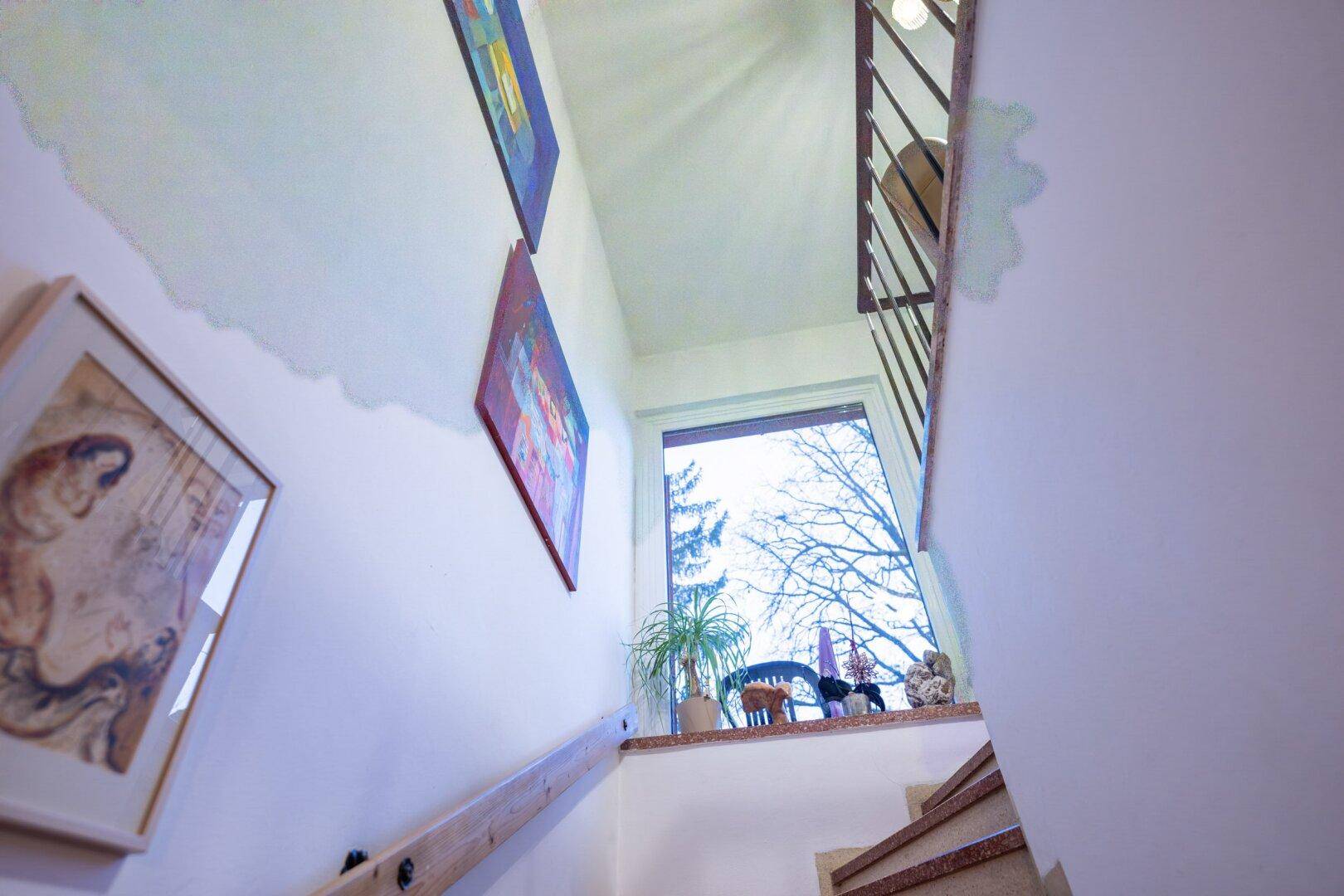 Treppenhaus mit Fenster und Holzgeländer, das Tageslicht hereinlässt.