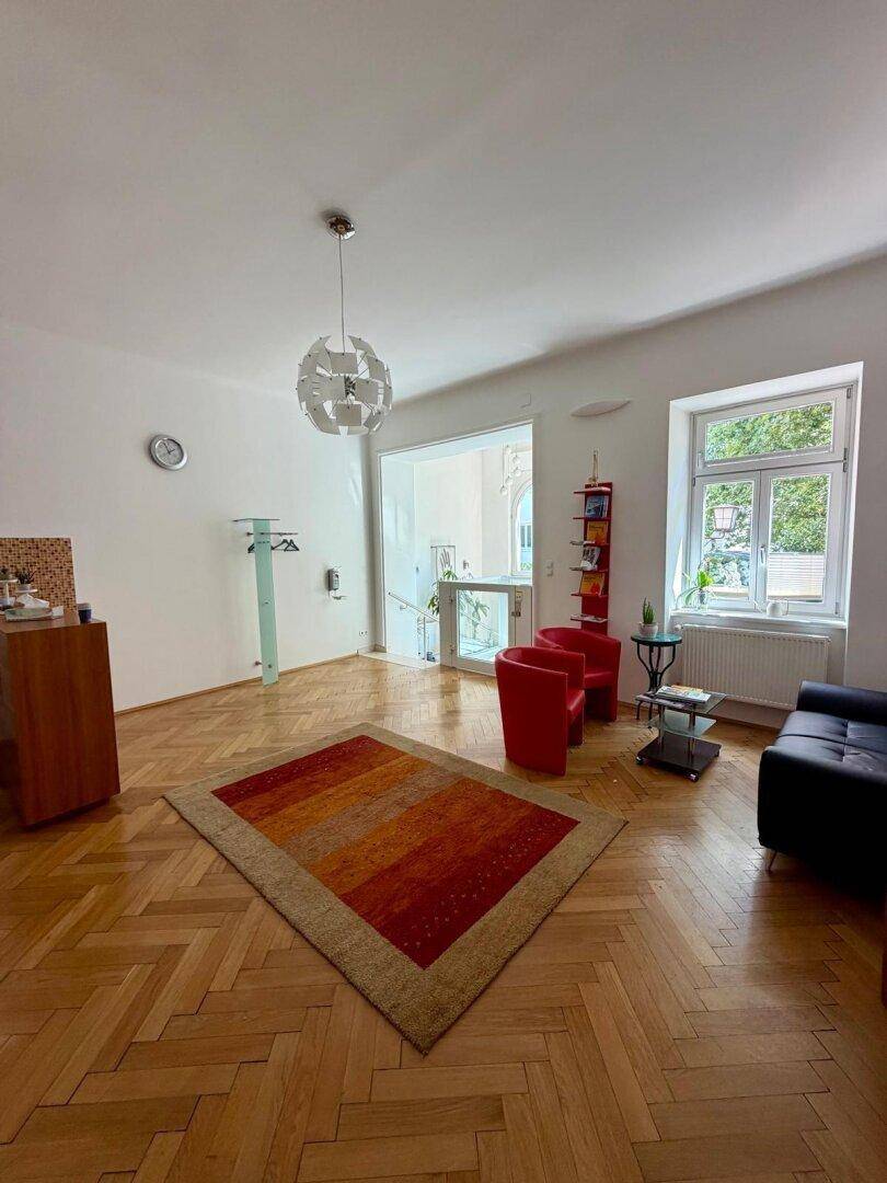 Geräumiger Wohnbereich mit Fischgrätparkett, großen Fenstern und viel Tageslicht, ideal für Empfänge.