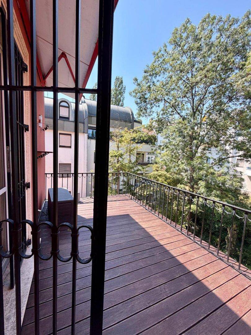Geräumiger Balkon mit Holzboden, schmiedeeisernem Geländer und Blick ins Grüne, perfekt zum Entspannen.