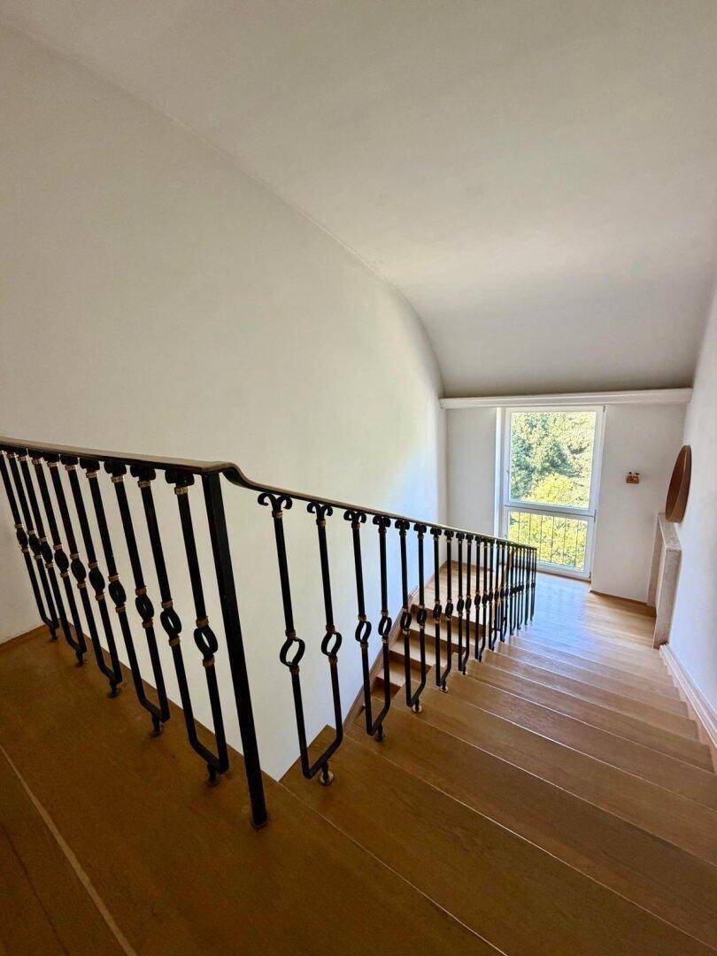 Elegantes Treppenhaus mit schmiedeeisernem Geländer und Holzstufen, verbindet die Etagen stilvoll.