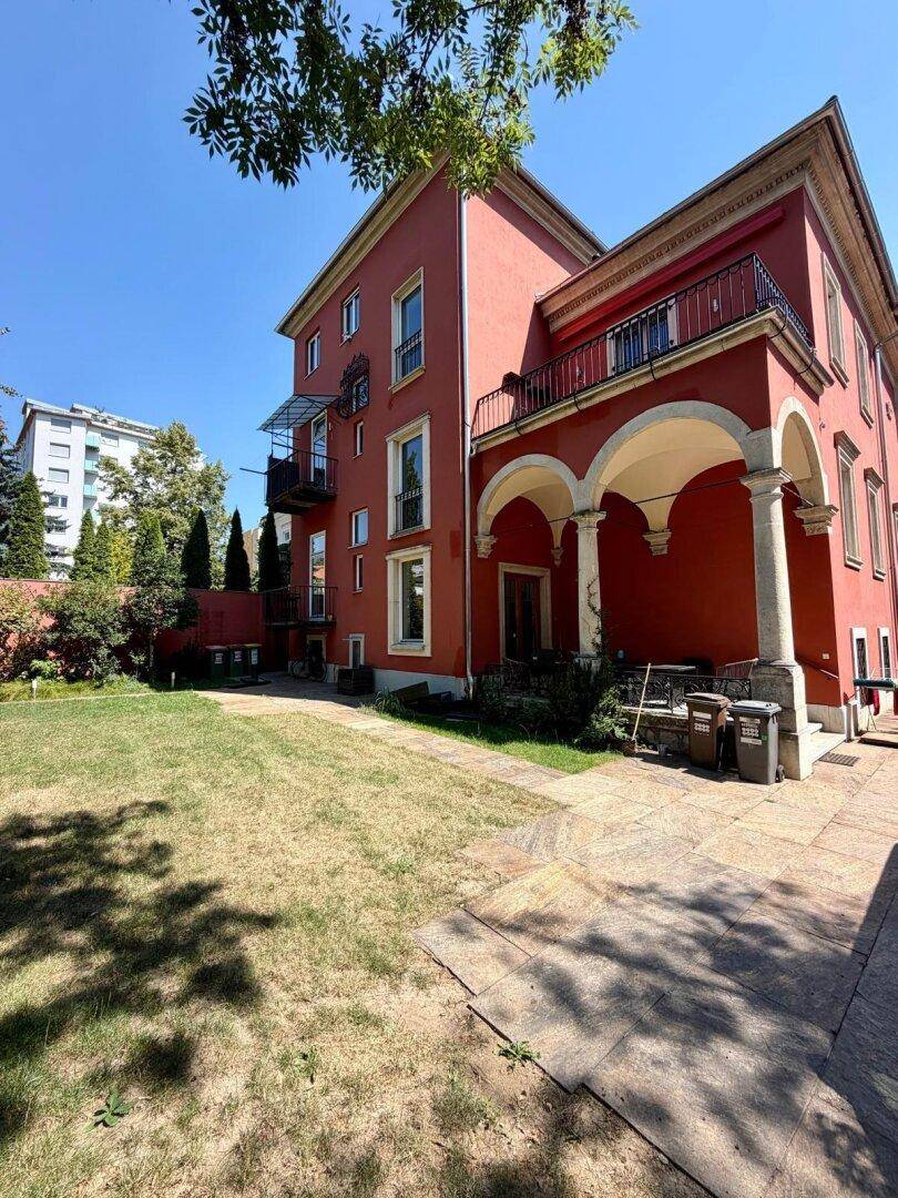 Rote Gründerzeitvilla mit großem Gartenbereich und Rasenfläche, bietet viel Platz im Freien.