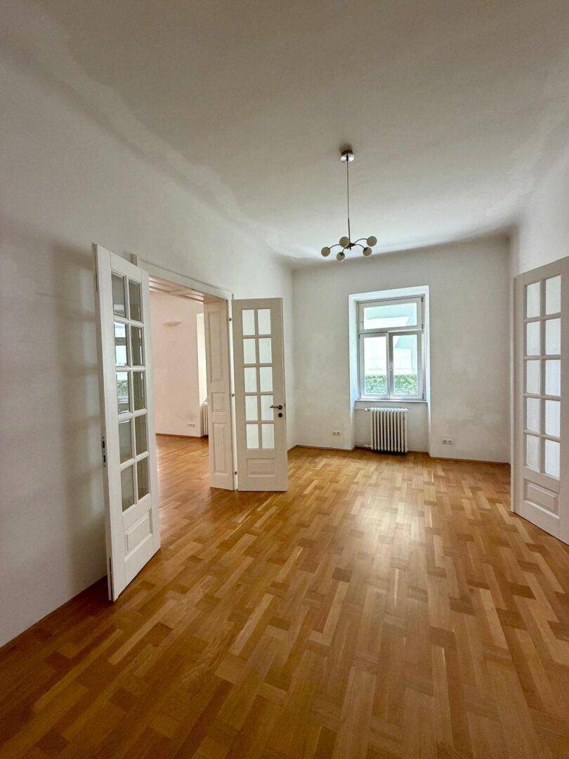 Leerer Raum mit Fischgrätparkett und eleganten Flügeltüren, bereit für individuelle Nutzung.
