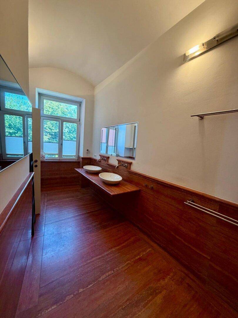 Geräumiges Badezimmer mit zwei Waschbecken, großem Fenster und warmen Holzelementen.