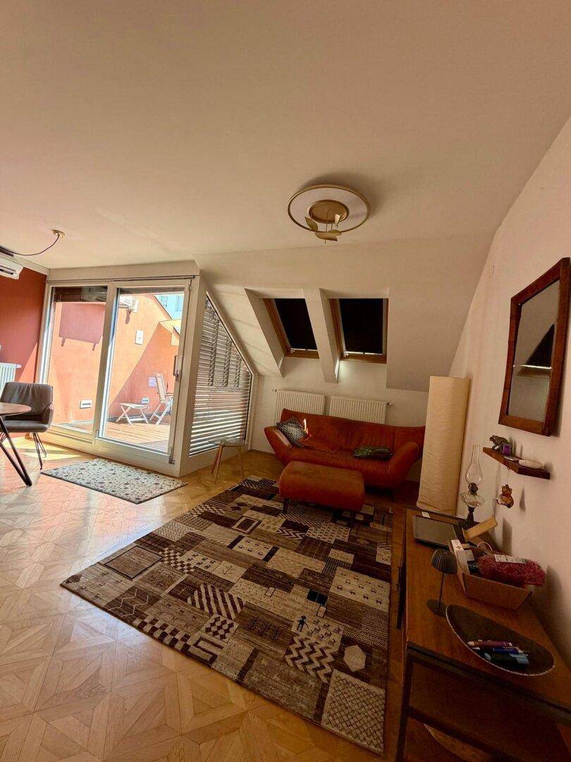 Gemütliches Wohnzimmer im Dachgeschoss mit Schrägen, Parkettboden und Zugang zur Terrasse.