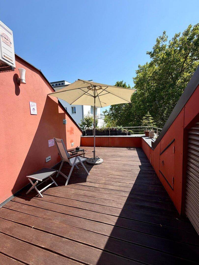 Sonnige Dachterrasse mit Holzbelag, Sonnenschirm und Sitzgelegenheiten, ideal zum Entspannen.