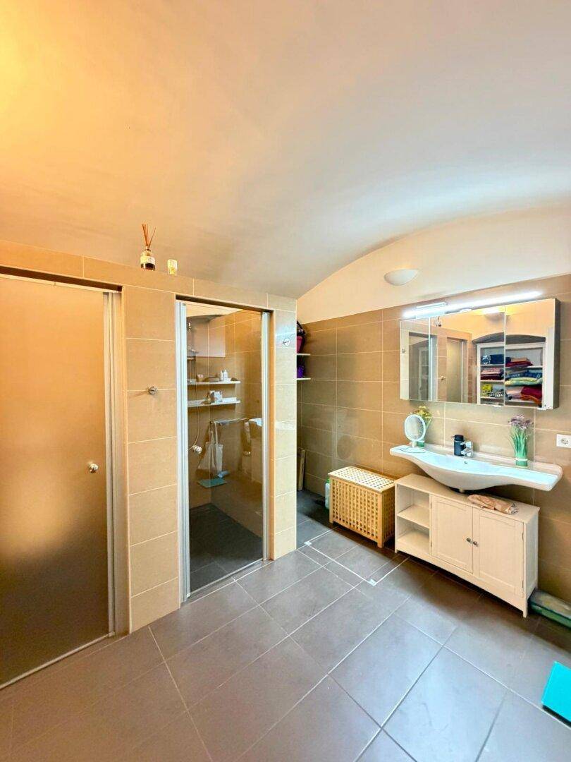 Badezimmer mit beigefarbenen Fliesen, einer Duschkabine und einem einzelnen Waschbecken.