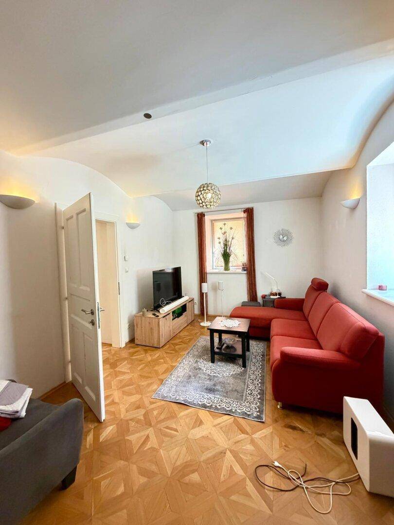 Gemütliches Wohnzimmer mit rotem Sofa, Fernseher und Parkettboden unter einer gewölbten Decke.