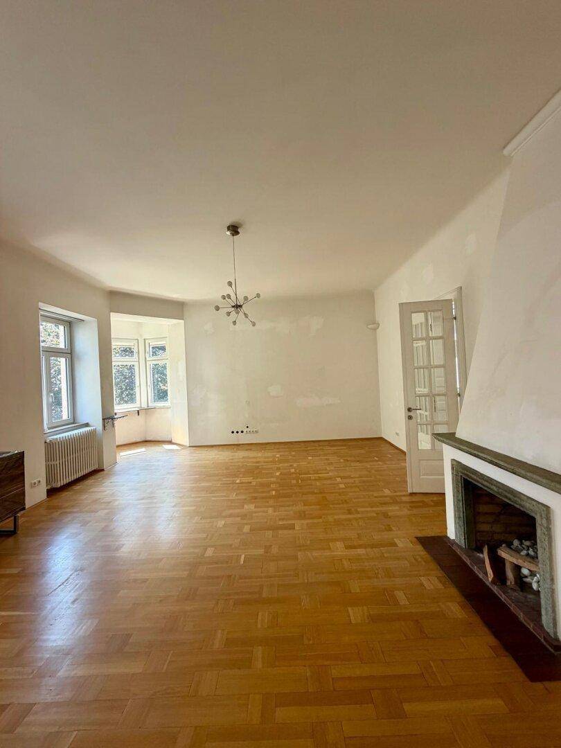 Geräumiges Wohnzimmer mit Parkettboden, Kamin und Erkerfenstern, bereit zur individuellen Gestaltung.