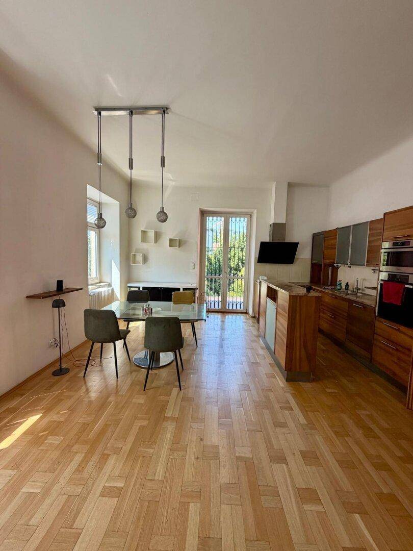 Moderne Holzküche mit Essbereich, Glasstisch und Zugang zu einem französischen Balkon.