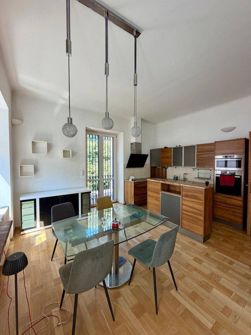 Helle Holzküche mit integriertem Essbereich, modernen Hängelampen und Zugang zum Balkon.