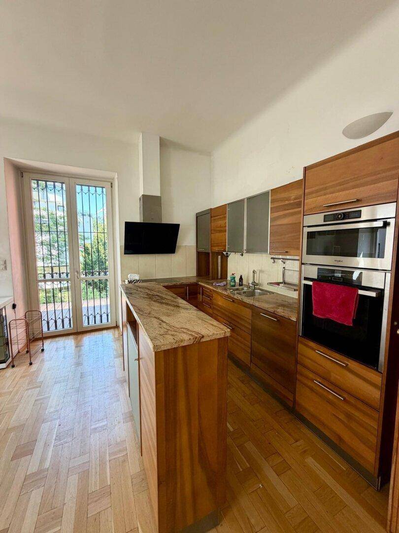 Geräumige Holzküche mit Granitarbeitsplatte, modernen Geräten und Zugang zu einem französischen Balkon.
