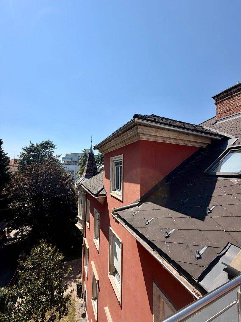 Dach und Seitenfassade der Gründerzeitvilla mit roten Wänden und Dachfenstern.