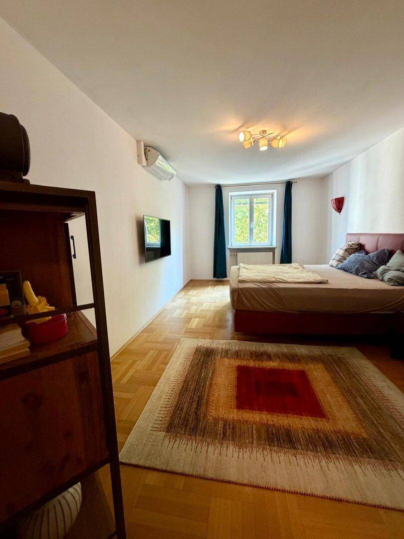 Schlafzimmer mit Parkettboden, Doppelbett, Fernseher und Klimaanlage für angenehme Temperaturen.