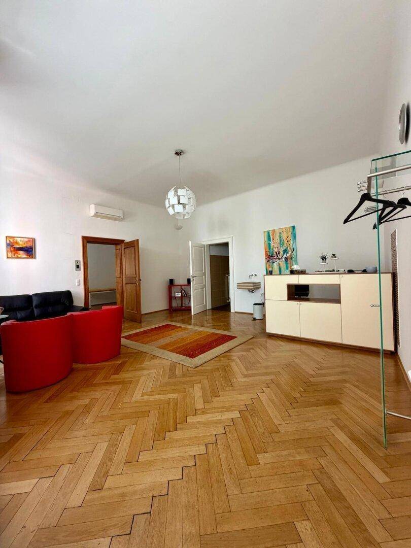 Helles Wohnzimmer mit Fischgrätparkett, roten Sesseln und einem modernen Deckenlicht.