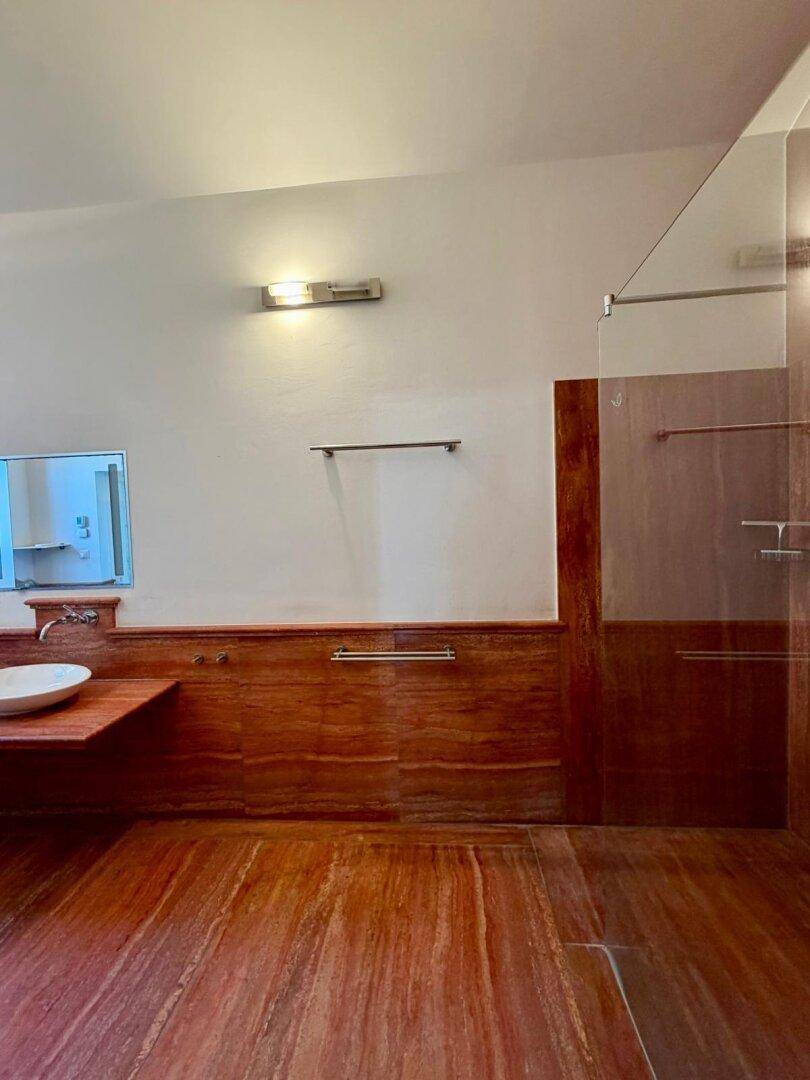 Modernes Badezimmer mit Holzverkleidung, Steinboden und Glasduschwand.