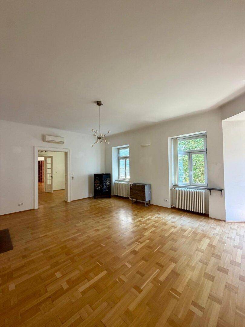 Geräumiges Wohnzimmer mit klassischem Parkettboden und viel Tageslicht.