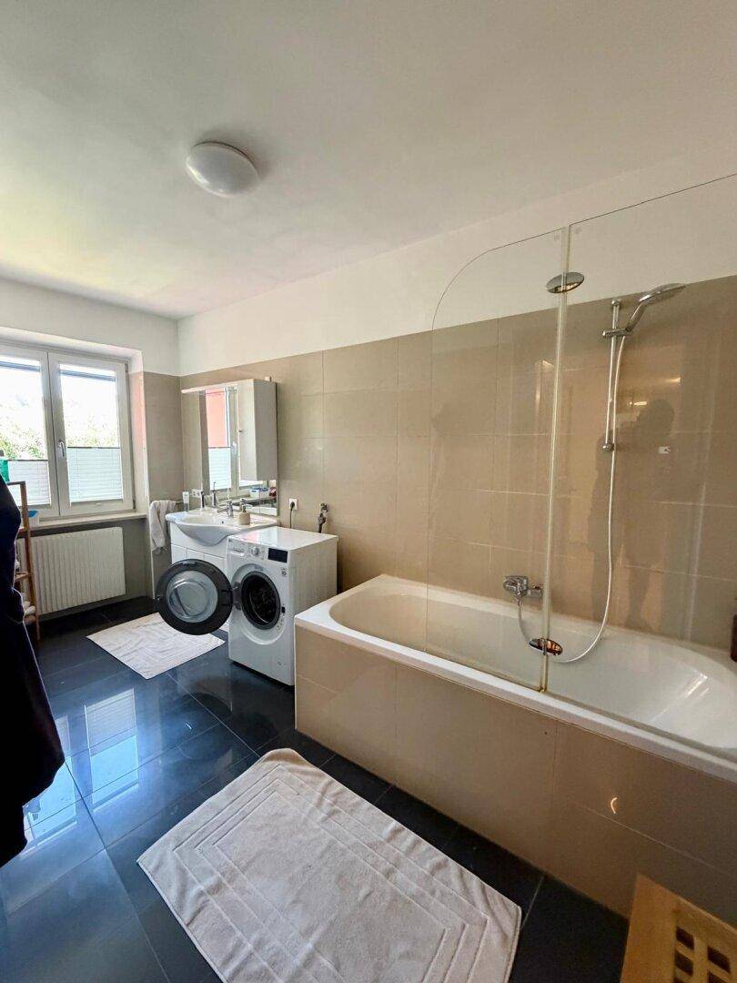 Badezimmer mit Badewanne, Dusche, Doppelwaschbecken und Waschmaschine.
