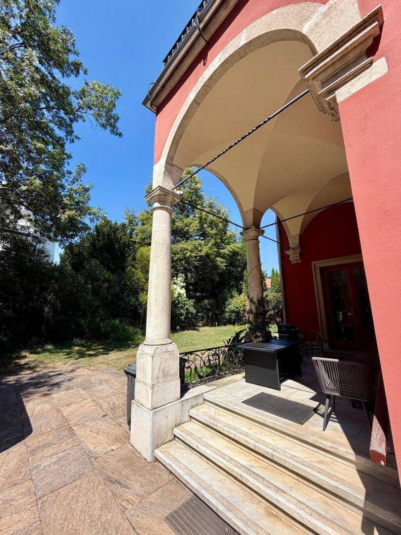Überdachter Eingangsbereich mit Säulen, Steintreppe und Blick in den Garten.