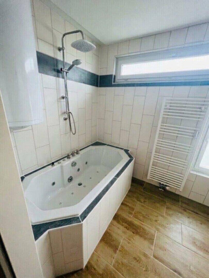 Helles Badezimmer mit Eckbadewanne, Regendusche, Fenster und beheiztem Handtuchhalter.