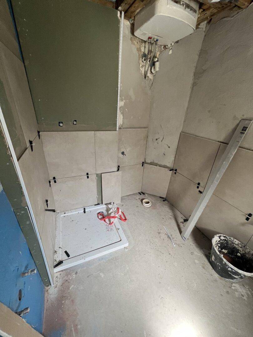 Badezimmer im Bau mit teilweise gefliesten Wänden und vorbereiteter Duschwanne.