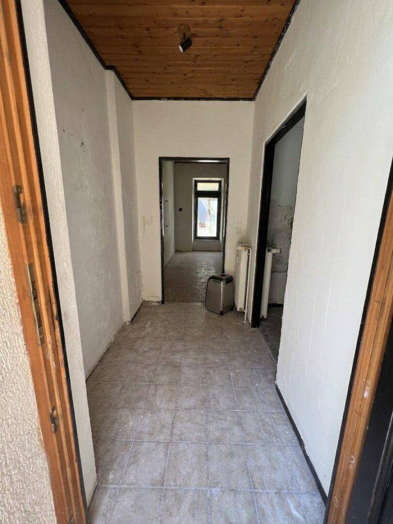 Langer Flur in Renovierung mit Holztürrahmen und Fliesenboden.