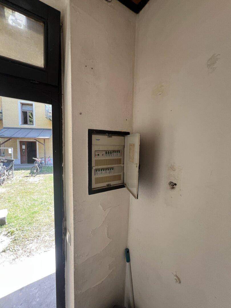 Eingangsbereich im Rohbau mit Sicherungskasten und Blick ins Grüne durch die Tür.
