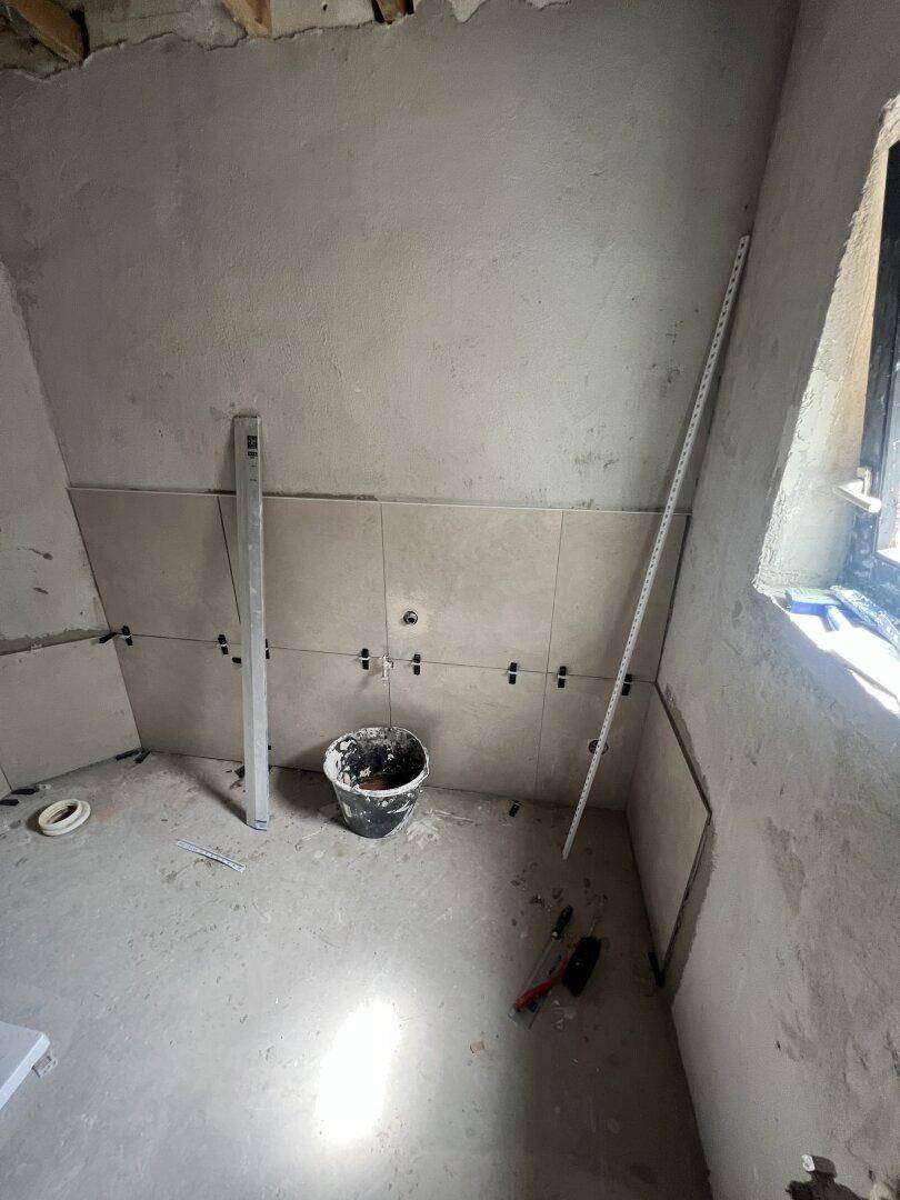 Badezimmer im Rohbau mit teilweise gefliesten Wänden und einem Fenster, bereit für den Ausbau.